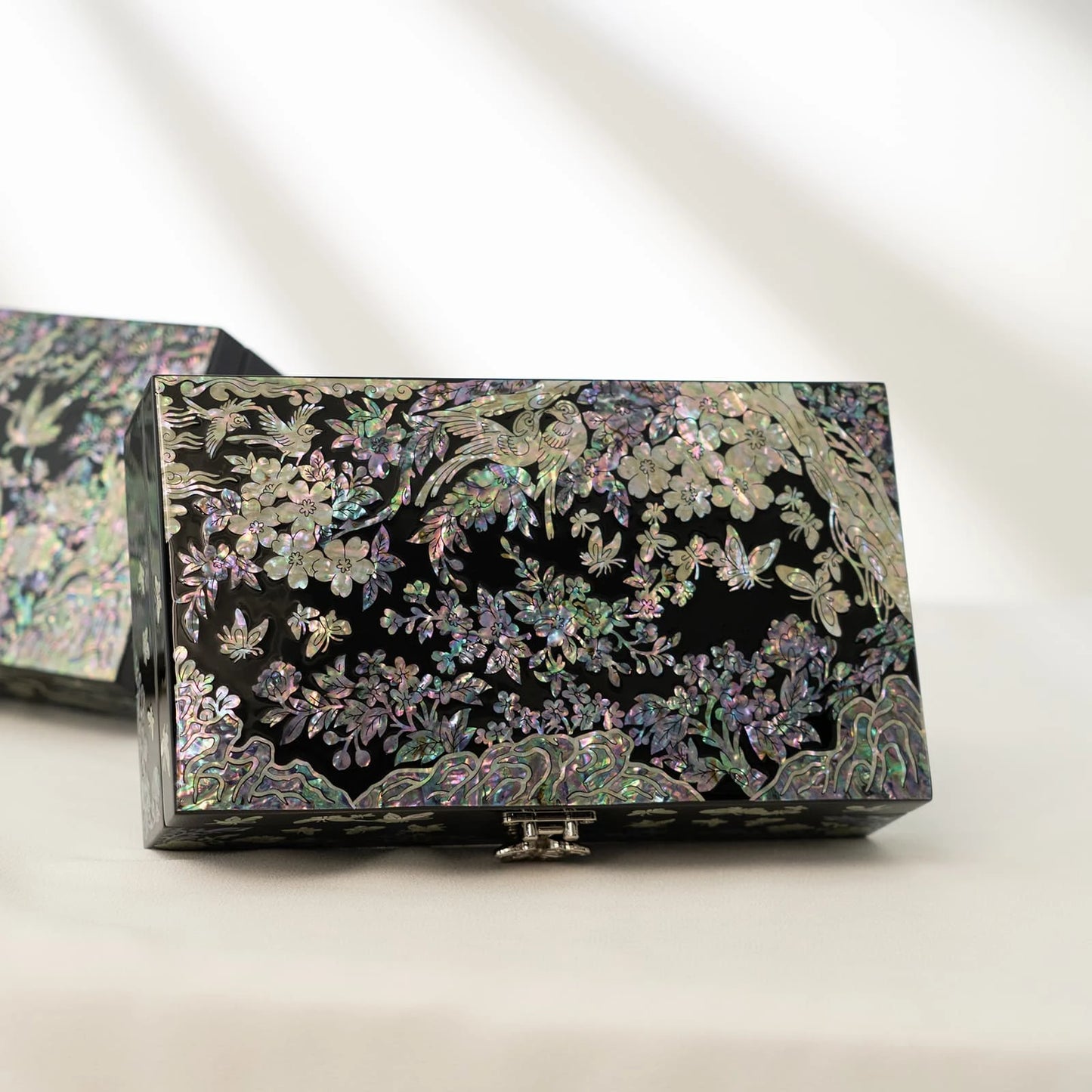Premium black lacquer jewelry box decorated with iridescent mother-of-pearl birds and floral tree motifs, resting on a white surface