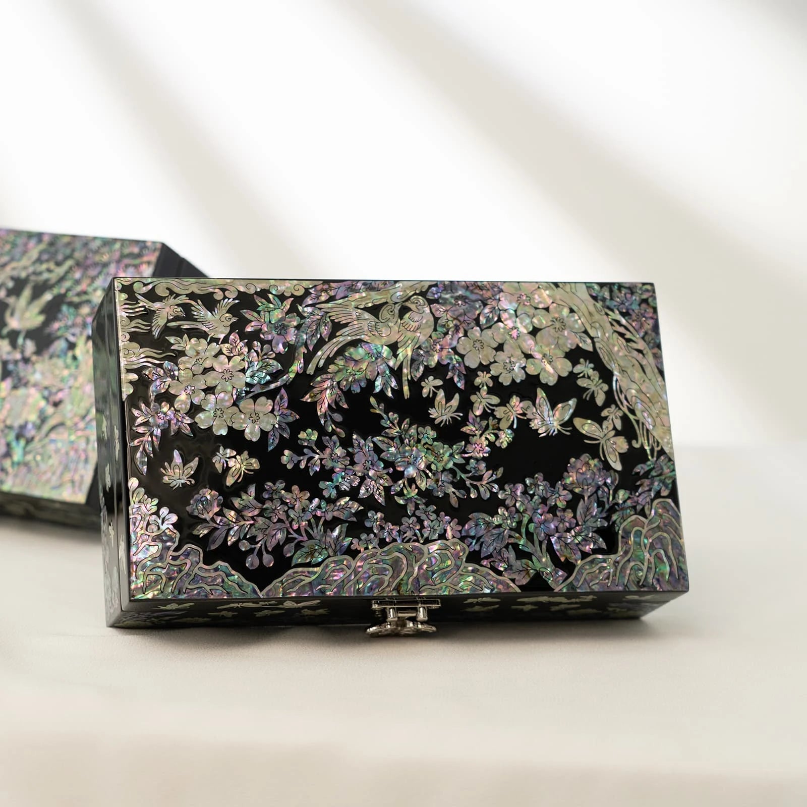 Premium black lacquer jewelry box decorated with iridescent mother-of-pearl birds and floral tree motifs, resting on a white surface