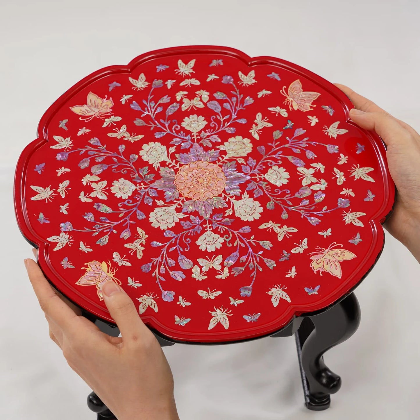 Red decorative tray with floral and butterfly patterns held by hands on a white background