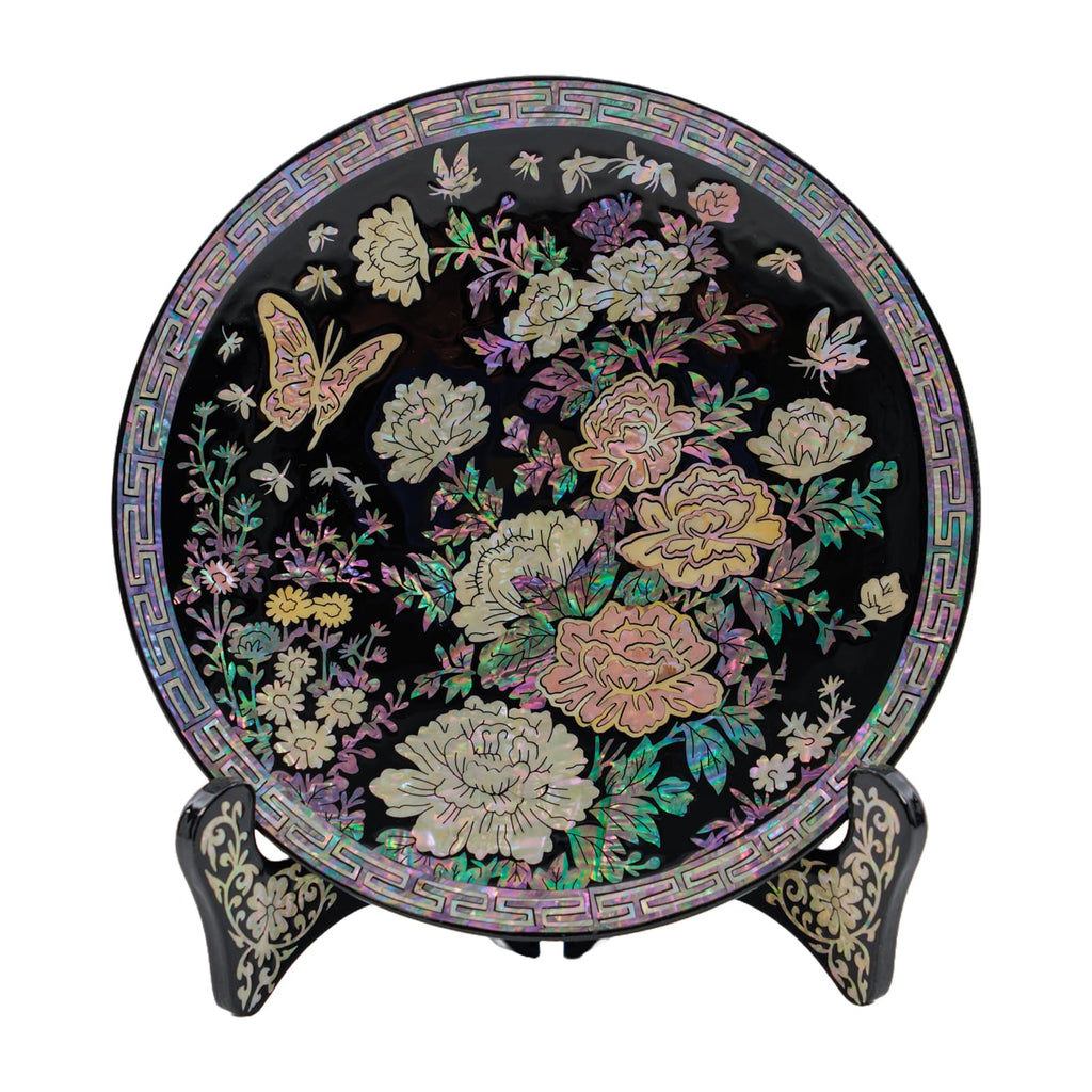 Round black lacquered decorative plate with mother-of-pearl floral inlay, displayed on an ornate stand.