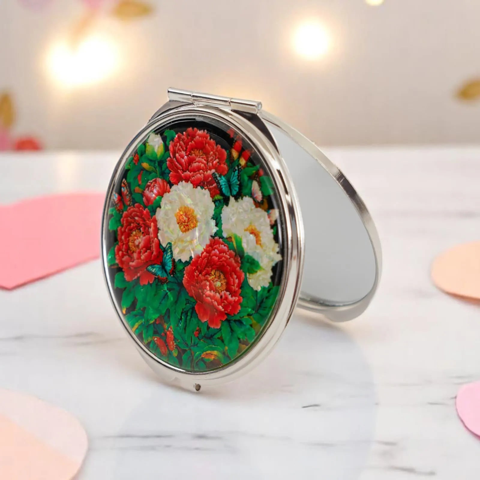 Round mother-of-pearl compact mirror with peonies, standing open on a table