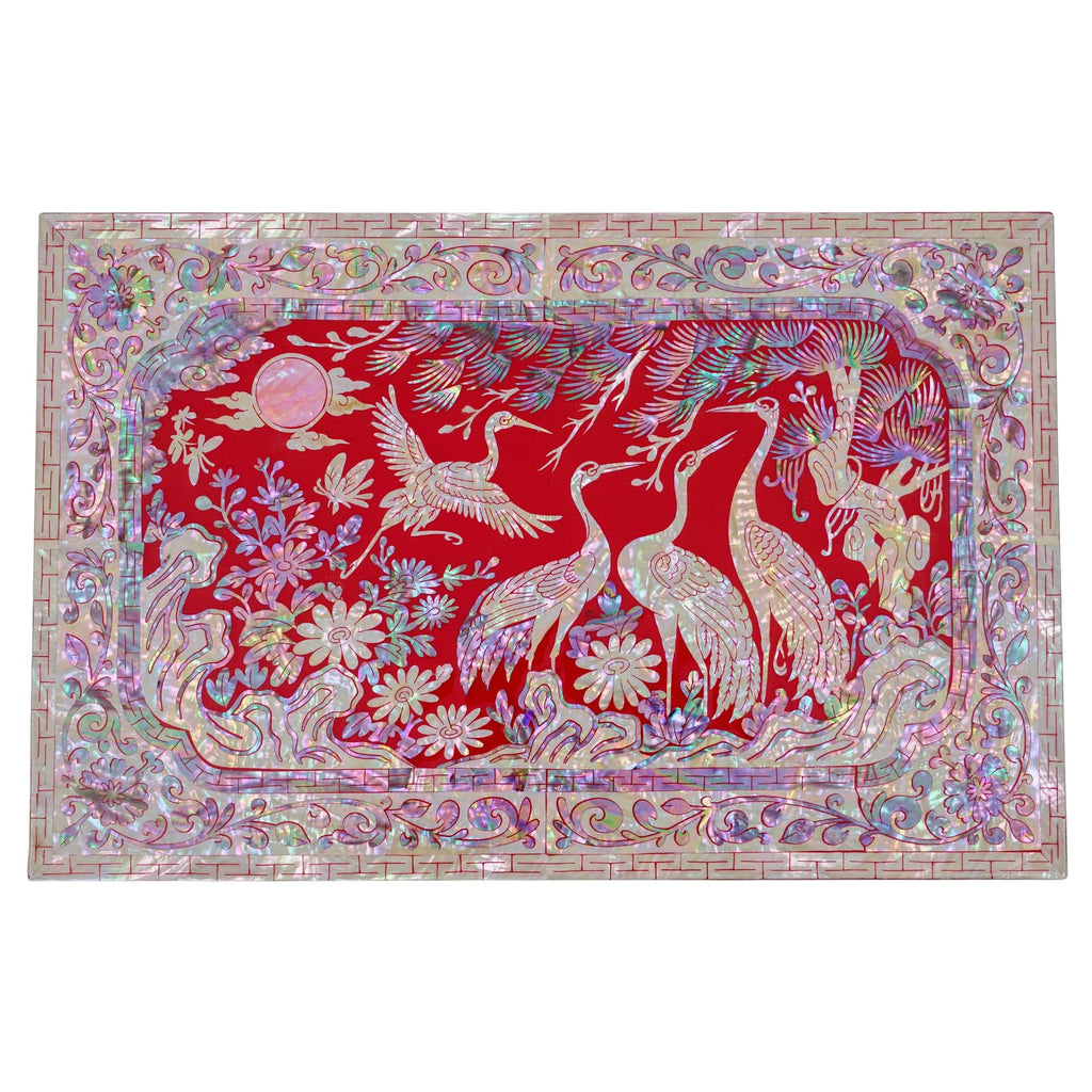 The top of a jewelry box with mother of pearl inlay, showcasing cranes and floral designs on a red backdrop, surrounded by a detailed border.