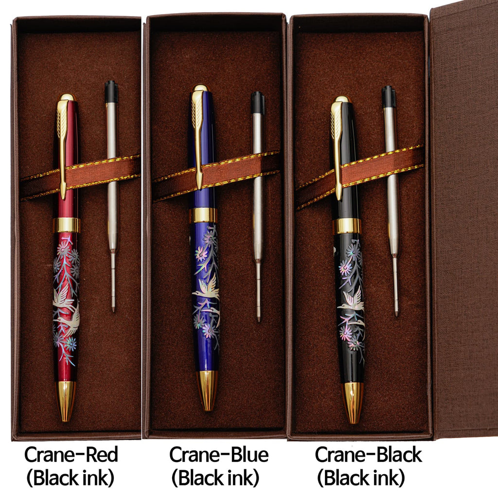 Three ballpoint pens with mother-of-pearl crane designs (red, blue, and black) are arranged in brown boxes with refills, labeled with their colors and ink types.