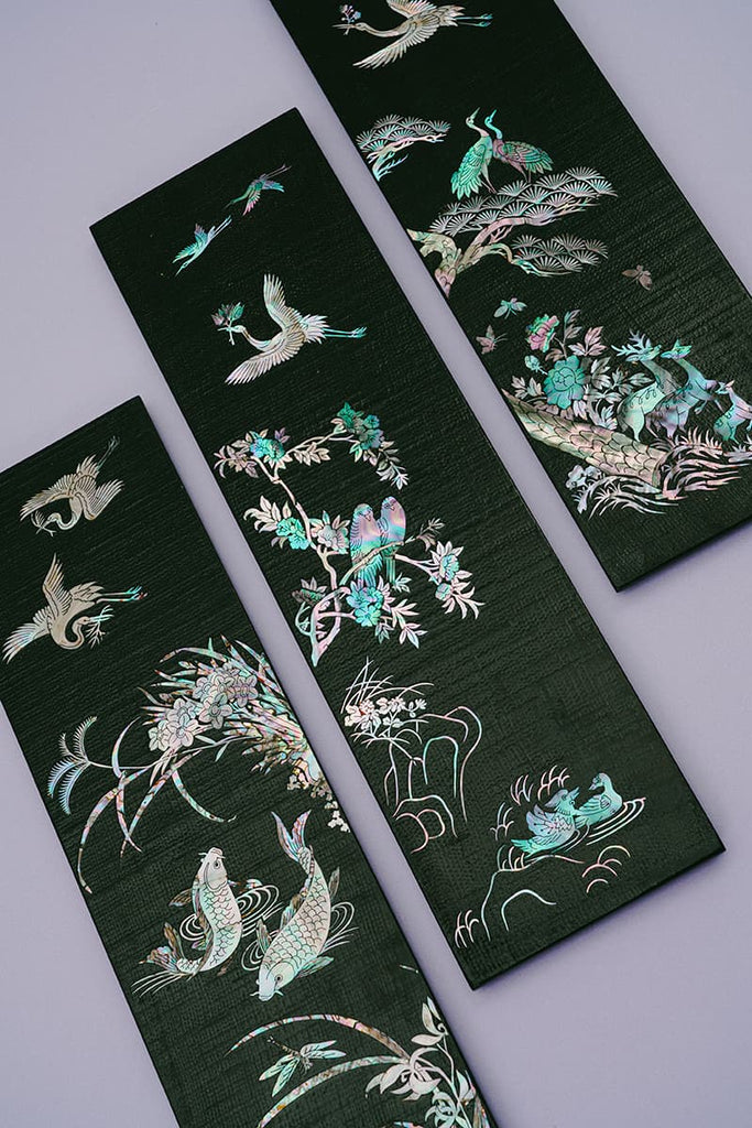 Three black wooden panels with mother-of-pearl inlay featuring birds, fish, and floral designs, displayed against a grey background.