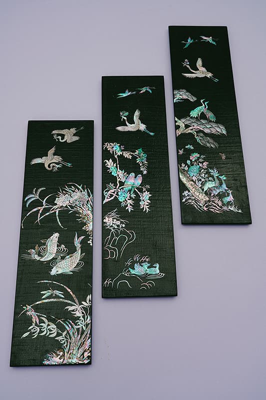 Three black wooden panels with intricate mother-of-pearl inlays of birds and fish, set against a purple backdrop.