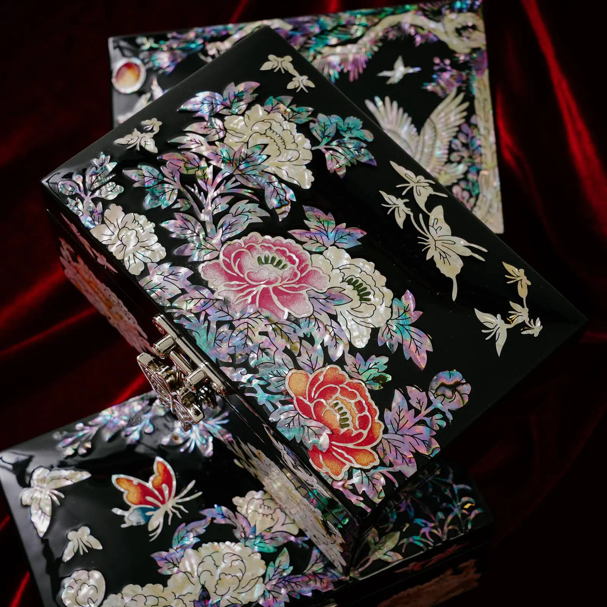 Two mother of pearl jewelry boxes on red velvet, peony and crane designs, close-up of butterfly clasp