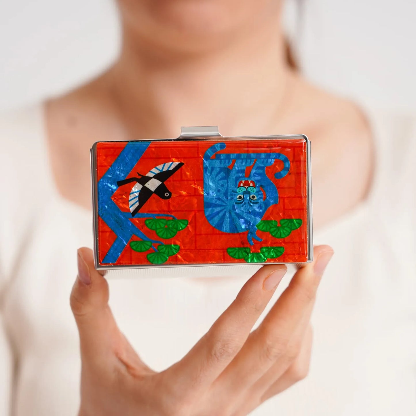 Woman holding a colorful case with a blue tiger and bird on a red background