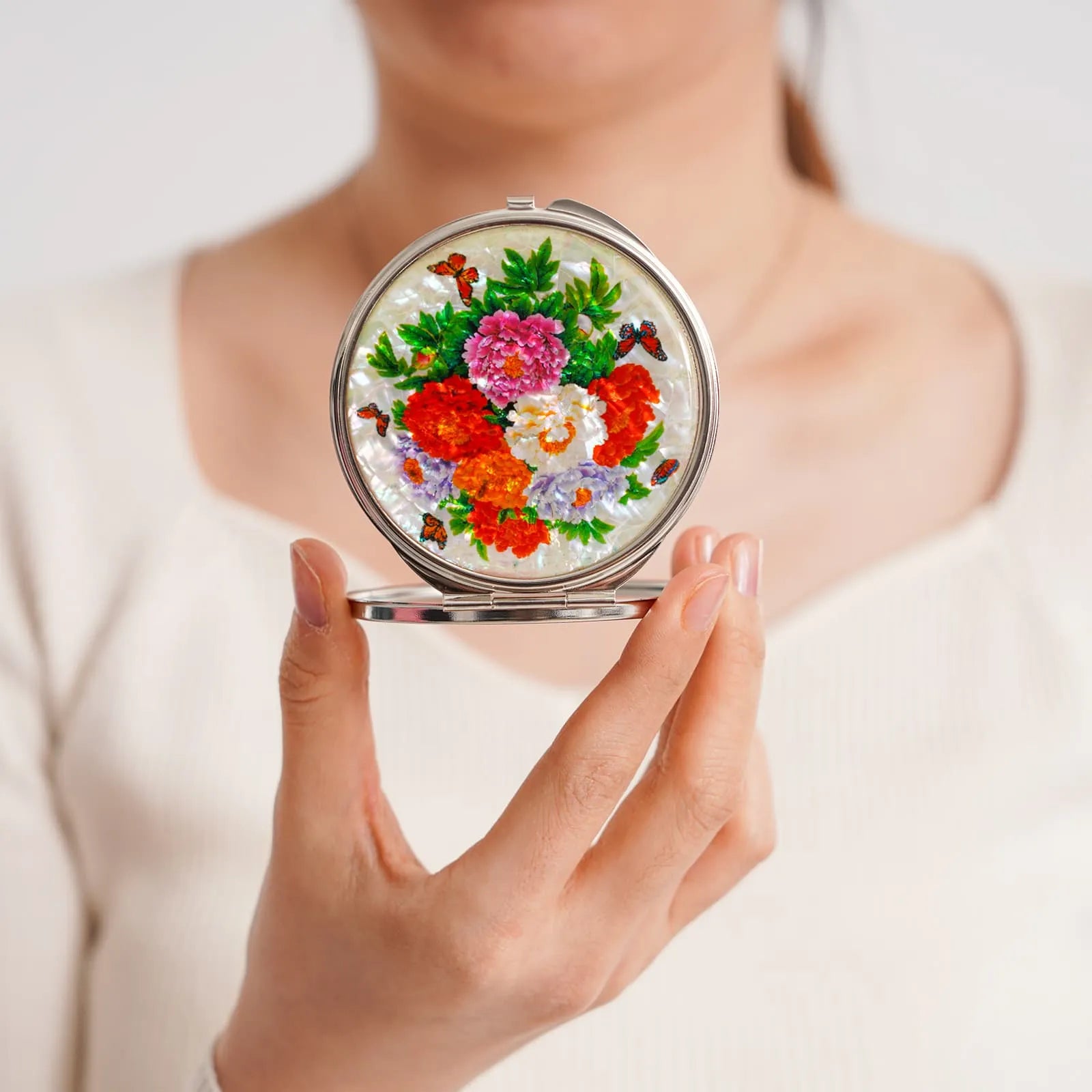 Woman holding a compact mirror with colorful peonies and butterflies