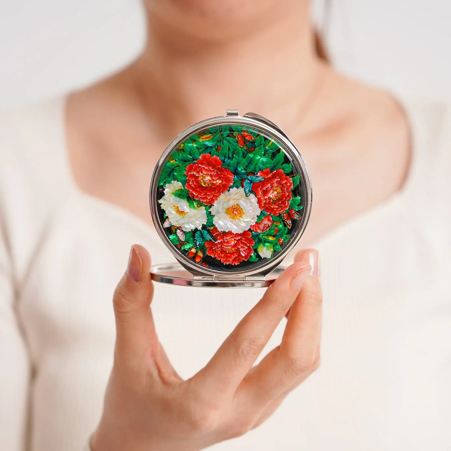 Woman holding a round mother-of-pearl compact mirror with colorful peonies