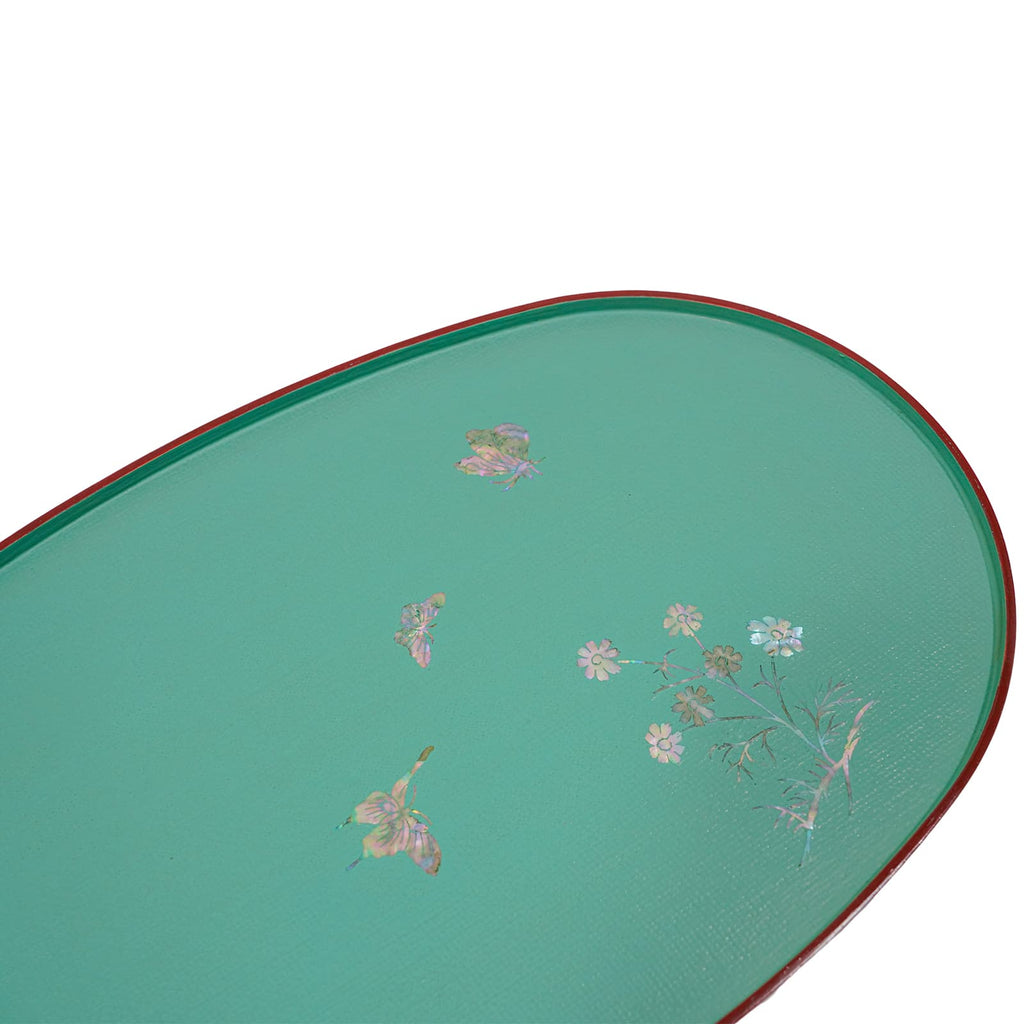 An angled view of a teal lacquered tray with a mother-of-pearl inlay of flowers and butterflies, edged in red.