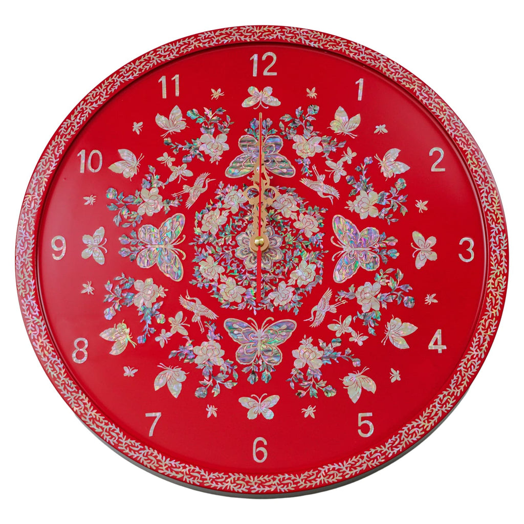 Vibrant wall clock with a rich red background, adorned with a mother of pearl design showcasing butterflies and flowers, and accented by gold hands. The clock's face is encircled by an intricate leaf pattern on the border.