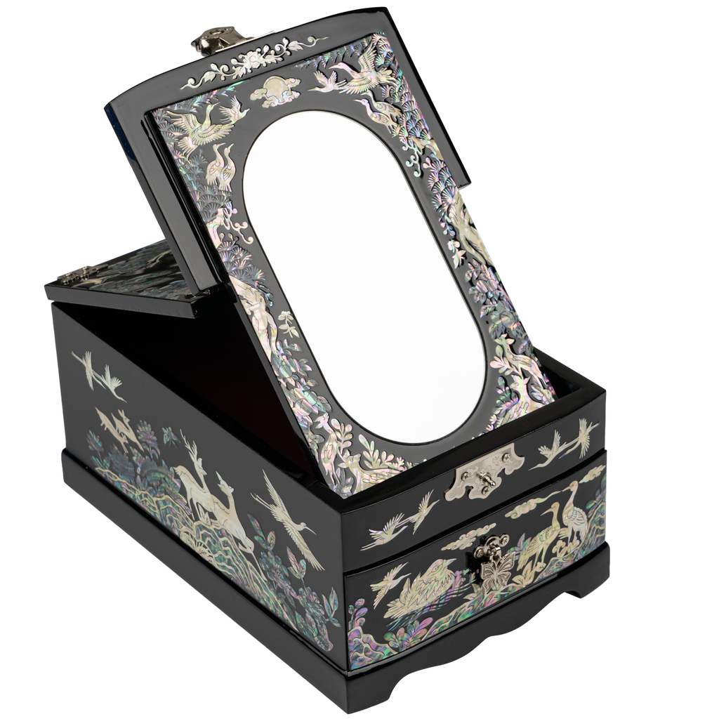 A jewelry box with mother-of-pearl inlay featuring crane and plant motifs, an open top lid with a built-in mirror, and a drawer, all on a black lacquer finish.