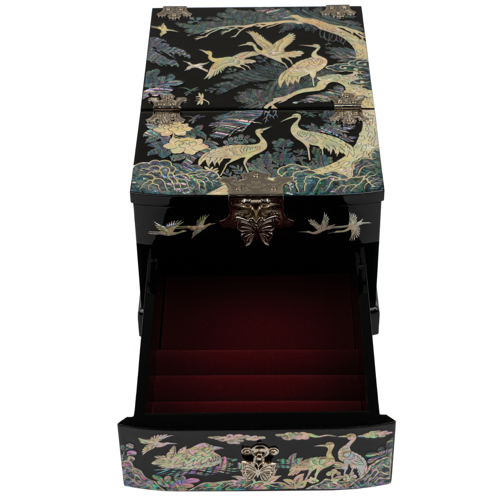 An open jewelry box with mother-of-pearl inlay displaying cranes and floral patterns on a black lacquer exterior, with velvet-lined tiers for storing jewelry.