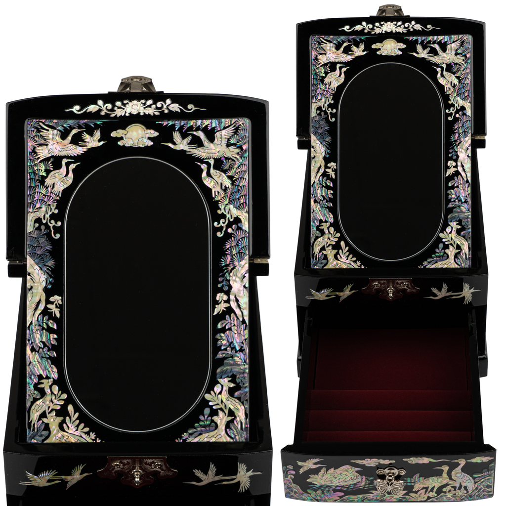 A black lacquered jewelry box with mother-of-pearl inlay, showing cranes and foliage, with a mirror inside the lid and a red-lined compartment.