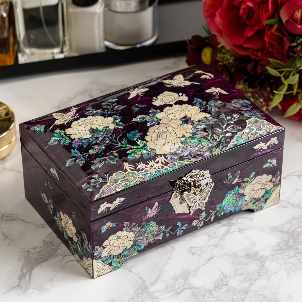 Decorative mother-of-pearl box with floral and butterfly designs, featuring a metal butterfly clasp, set on a marble surface with a red bouquet in the background.