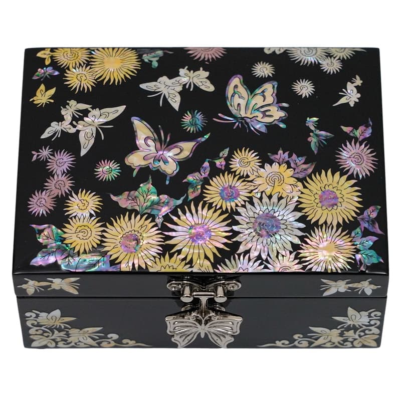 A close-up of a jewelry box with a vivid floral and butterfly motif in mother-of-pearl on a black background, featuring a butterfly-shaped clasp