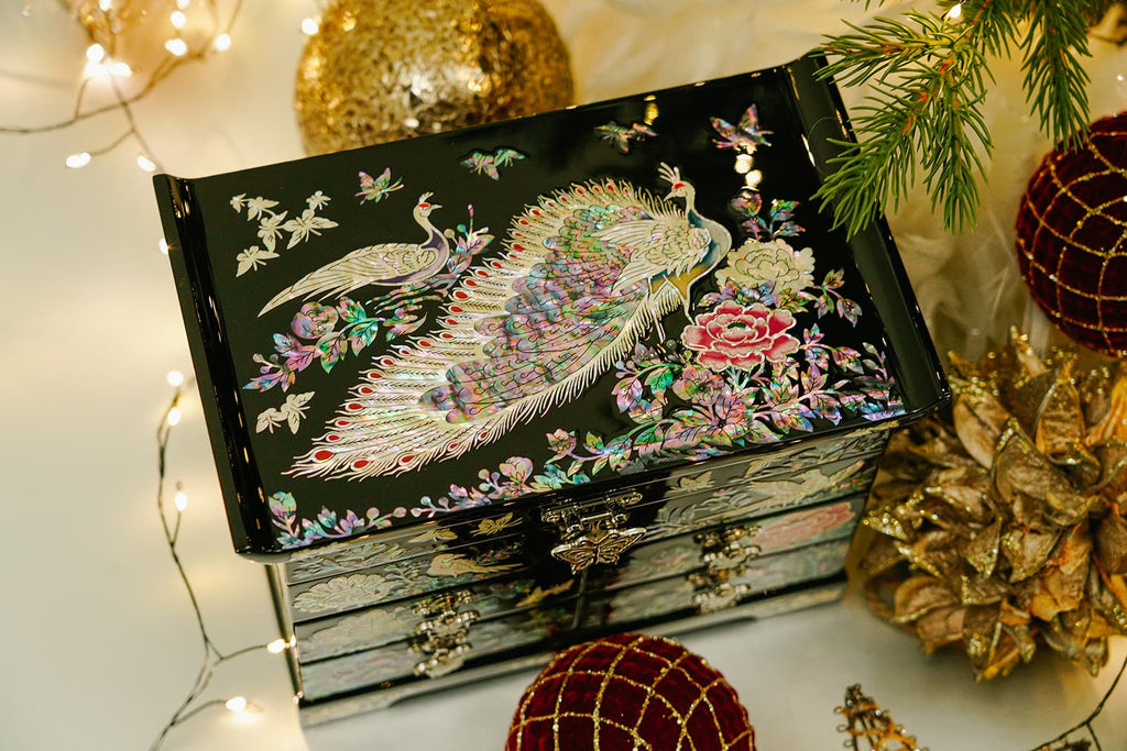 A jewelry box with peacock and floral mother-of-pearl inlay, against a black lacquer background, illuminated by soft lights.