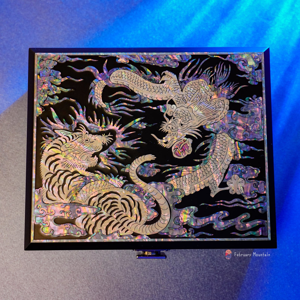  A decorative box with a tiger and dragon mother of pearl inlay, displayed against a blue light, with the February Mountain logo.
