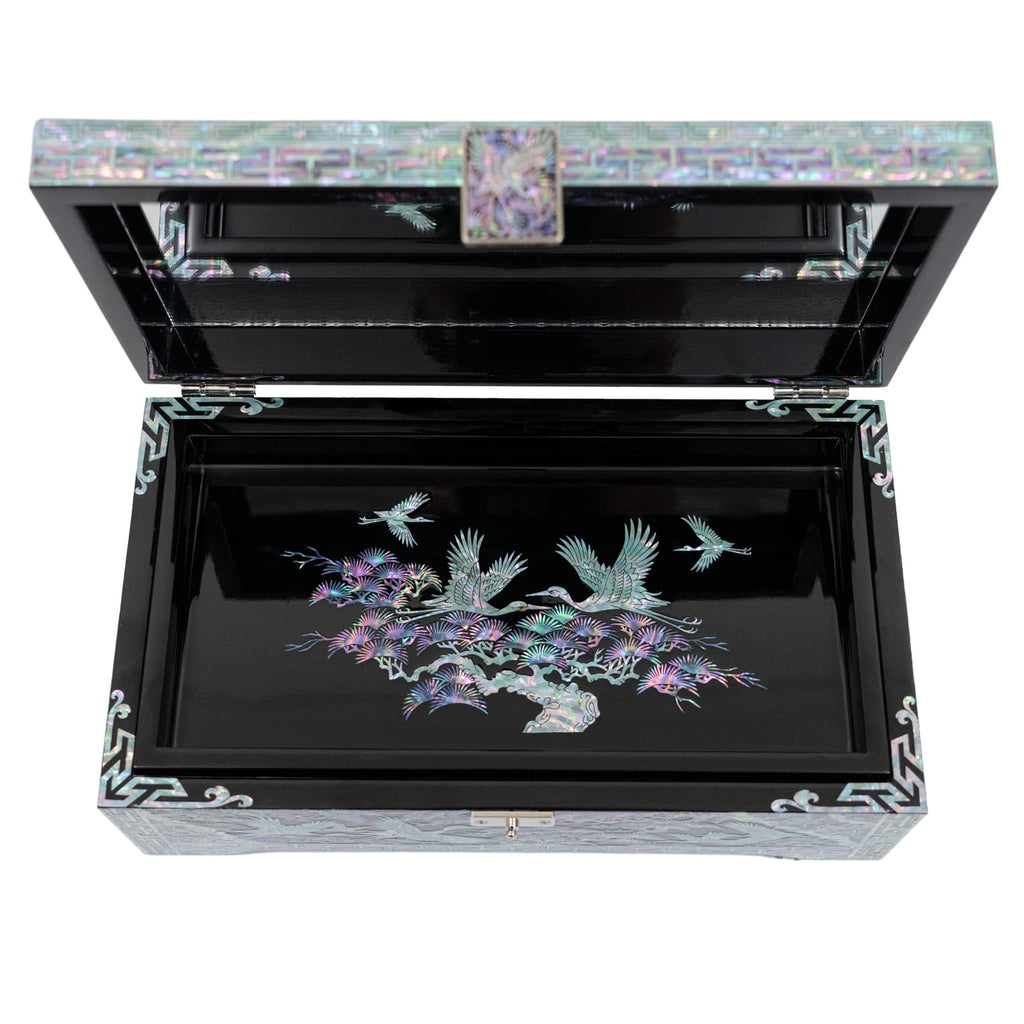 An open jewelry box with a detailed tray showcasing a black background and colorful inlay of pine trees and cranes is visible