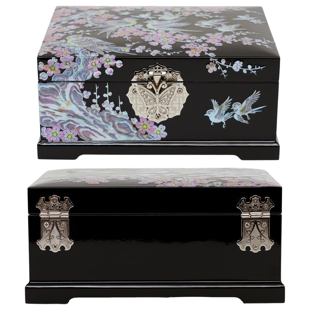  A black lacquered jewelry box with a marbled mother of pearl design on top and birds on the front, featuring ornate metallic clasps shaped like a butterfly and a crest.
