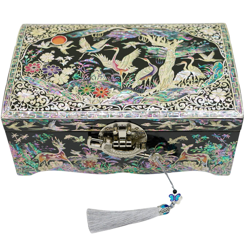 A closed jewelry box with a mother-of-pearl design featuring cranes and flowers, a traditional lock, and a tasseled key hanging in front.